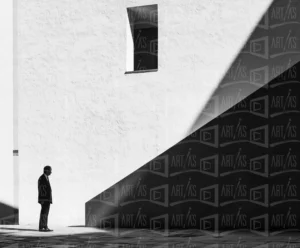 Fotografía en blanco y negro de un hombre de pie frente a una pared con sombras marcadas. | CUADROS DE ATREZZO PARA CINE Y PUBLICIDAD