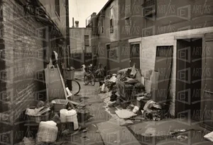 Escena urbana de un callejón con basura y un hombre revisando entre los desechos. | CUADROS DE ATREZZO PARA CINE Y PUBLICIDAD